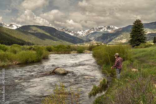 Photography A person, mature, Caucasian, fly fishing on a river with view of snow covered mo