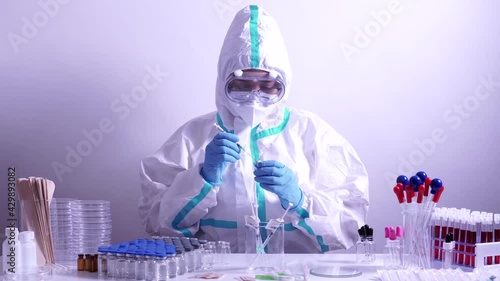 Doctor or nurse in full ppe suit preparing syringe with Covid 19 vaccine. Vaccination against coronavirus in the hub. Equipped laboratory with many vaccine vials and tools. photo