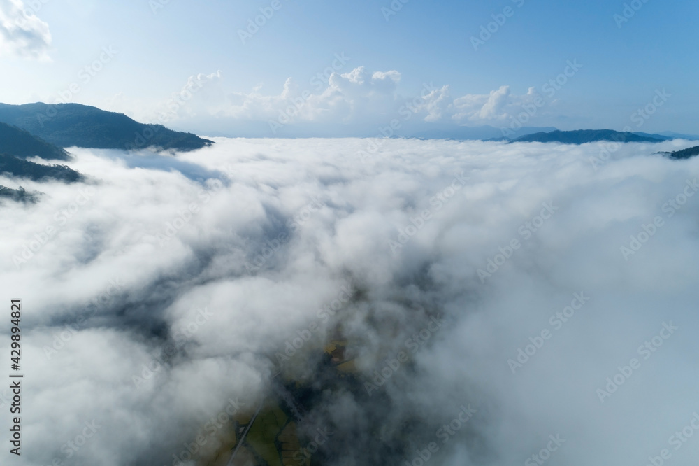 Aerial view drone shot of flowing fog waves on mountain tropical rainforest,Bird eye view image over the clouds Amazing nature background with clouds and mountain peaks in Nan Thailand