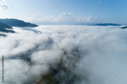 Aerial view drone shot of flowing fog waves on mountain tropical rainforest,Bird eye view image over the clouds Amazing nature background with clouds and mountain peaks in Nan Thailand