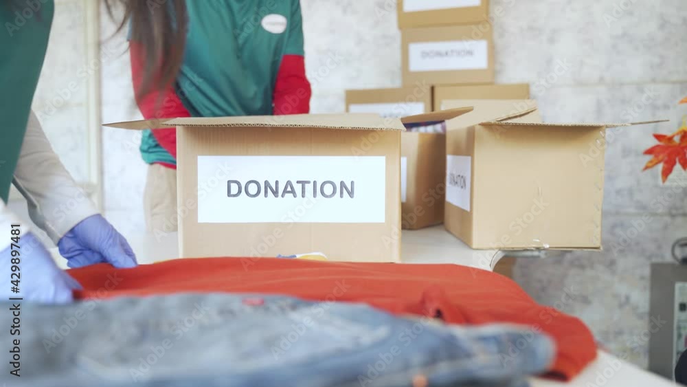 unrecognizable volunteers busy working by folding clothes and placing inside the donation boxes