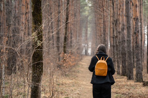  A girl with a phone in her hands and headphones in her ears is walking along a path in a pine forest.