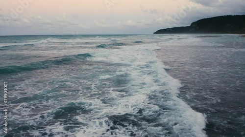 Slow motion Aerial Skimming Across waves panning out to the ocean