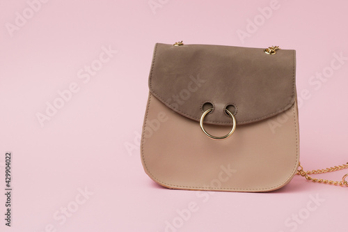 Women's suede bag with a gold ring on the lock on a pink background.