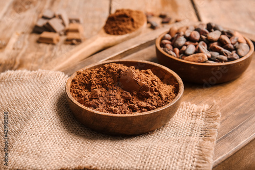 Bowls with cocoa powder and beans on wooden background