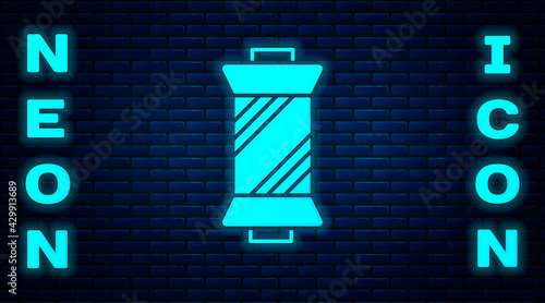 Glowing neon Sewing thread on spool icon isolated on brick wall background. Yarn spool. Thread bobbin. Vector