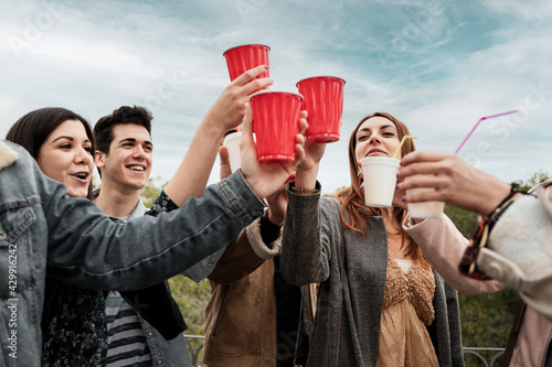 Outdoors friends party. Young people celebrating friendship toasting with beers in plastic ware red cup having fun and drinking together in the park