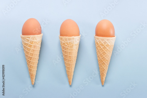 Easter composition with three waffle cones with three brown eggs on blue background