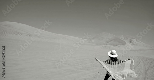 Monochrome image of a woman putting on her scarf on the windy day at Huacachina desert in Ica region, Peru, South America