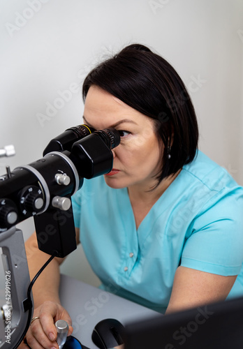 Health care, medicine, people, eyesight and technology concept. Female optician looks at special modern equipment for eye sigth testing. Closeup. photo