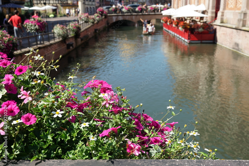 Colmar, France is known as city in blossom. Detail of water channel with a bridge in the background. Everywhere there are tourists and the terrace restaurants are full of people in summer 2020. 