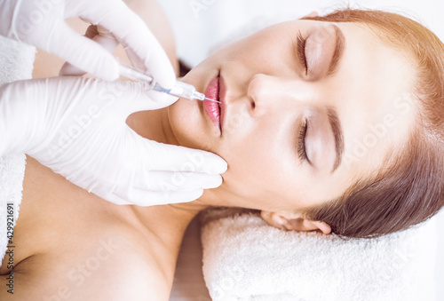 Beautician doing beauty procedure with syringe to face of young brunette woman in sunny spa center. Cosmetic medicine and surgery  beauty injections