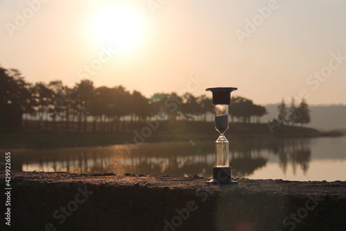 Hourglass in the dawn time. Hourglass on the background of the lake and the rising sun.