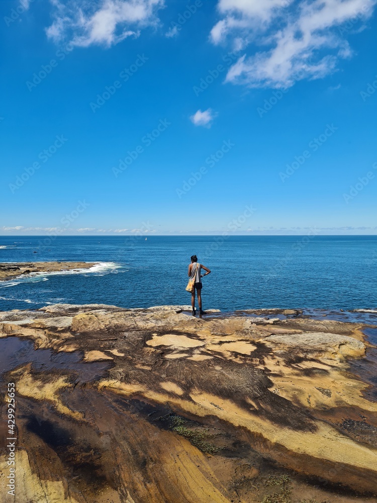 Girl standing at ultra blue ocean lookout cliff at edge of coastline at national park in Australia. Vivid blue ocean view in Australian summer. 