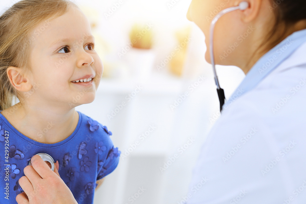 Doctor examining a little girl by stethoscope. Happy smiling child patient at usual medical inspection. Medicine and healthcare concepts Doctor examining a little girl by stethoscope. Happy smiling child patient at usual medical inspection. Medicine and healthcare concepts