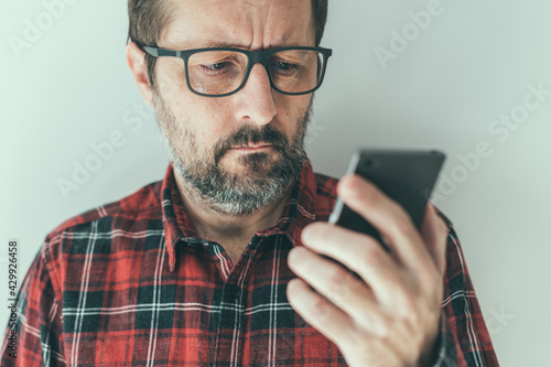 Headshot portrait of mid-adult male reading text message notification on mobile smart phone