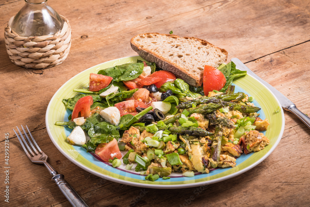 American fried scrambled eggs with asparagus, spinach and tomatoes in a large plate on a rustic wooden table - a simple rustic breakfast