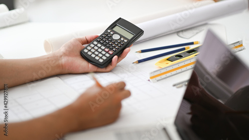Hand holding a calculator and pencil checking house plans, engineers are calculating the house scale.