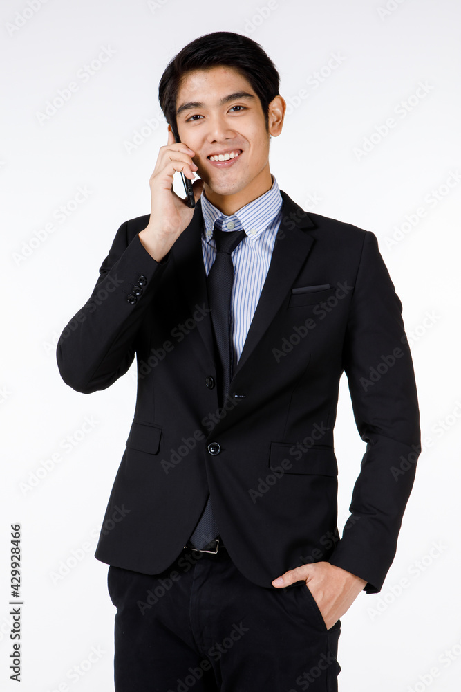 Portrait shot of Asian young happy handsome smart office worker leader in black formal suit with necktie standing smiling talking with client on mobile smartphone in hand in front of white background Portrait shot of Asian young happy handsome smart office worker leader in black formal suit with necktie standing smiling talking with client on mobile smartphone in hand in front of white background