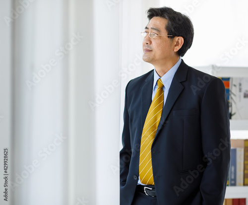 Portrait shot of Asian senior old successful company entrepreneur in formal suit with brown necktie and golden eyeglasses standing  against white background