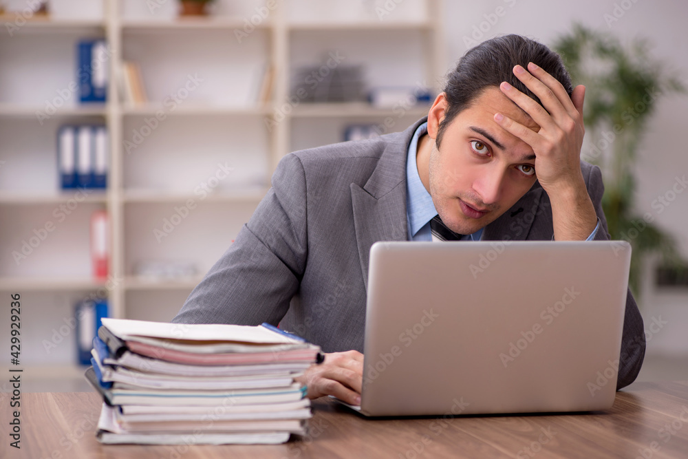 Young male employee unhappy with excessive work in the office Young male employee unhappy with excessive work in the office