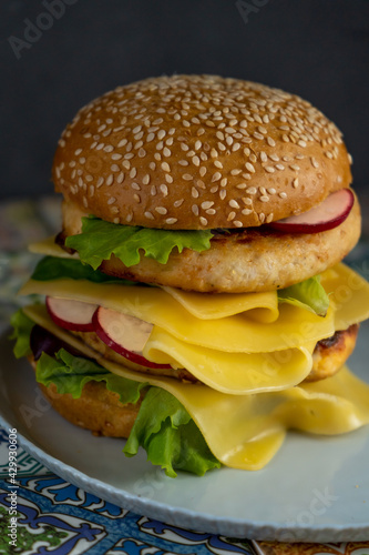 Hamburger bun, double chicken cutlet with cheese, lettuce, arugula and radish. Meat, vegetables and bread. Ingredients. Homemade burger on a plate. Table made of colored tiles