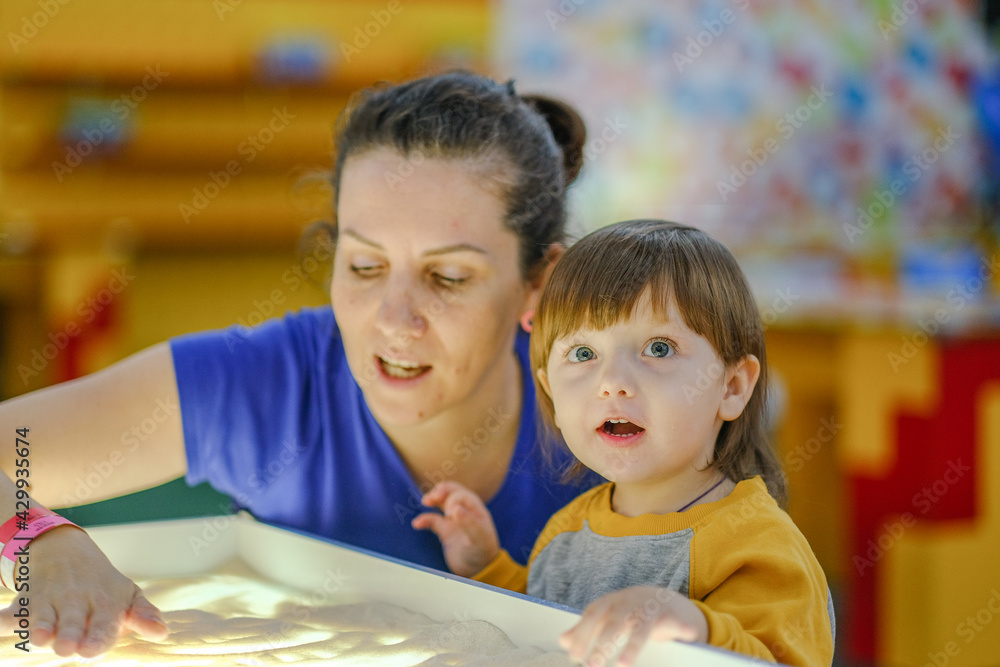 Creative early baby development. A mother teaches her child to draw with her fingers in the sand. Center for the Development of Children with Autism. Creative early baby development. A mother teaches her child to draw with her fingers in the sand. Center for the Development of Children with Autism.