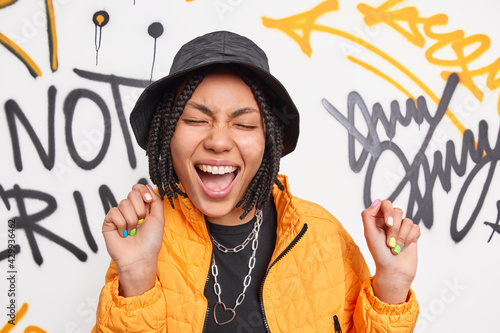 Valokuva Urban stylish female teenager dances carefree with happy expression against graf
