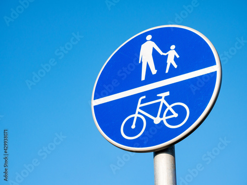 Divided path for cyclists and pedestrians blue road sign, object detail, closeup, isolated on blue sky background. City signs, symbols, shared road for bikers and pedestrians transportation concept