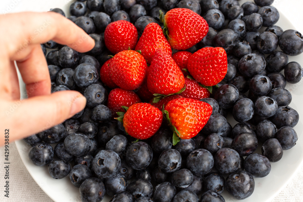 hand reaches for a plate of blueberries and strawberries hand reaches for a plate of blueberries and strawberries