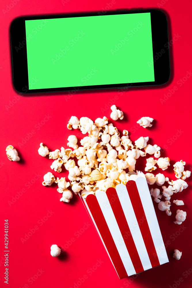 Popcorn Striped Cinema Box on Red Background. Smartphone with Green Screen Mockup Template. Flat Lay Ddesign. Digital Content Streaming Platforms.