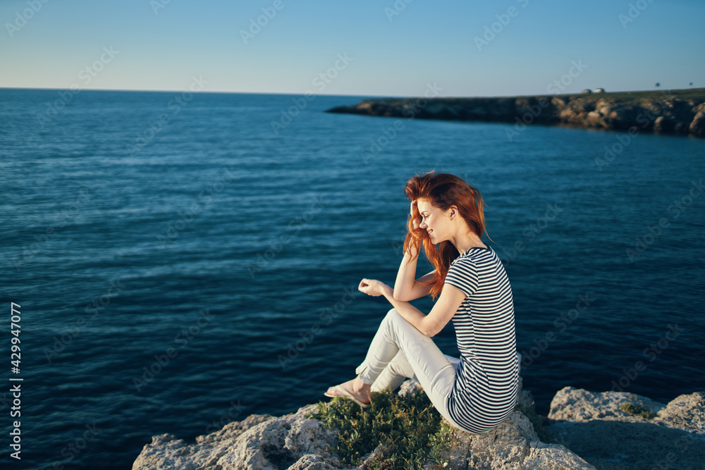 Naklejka premium woman in a t-shirt and trousers sits on a rock on the beach near the sea top view