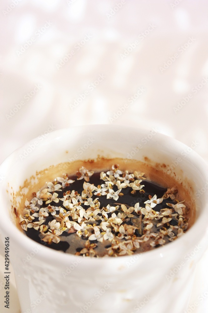 Taza blanca de porcelana labrada con café con flores del olivo sobre tejido blanco en un fondo luminoso. Taza blanca de porcelana labrada con café con flores del olivo sobre tejido blanco en un fondo luminoso.