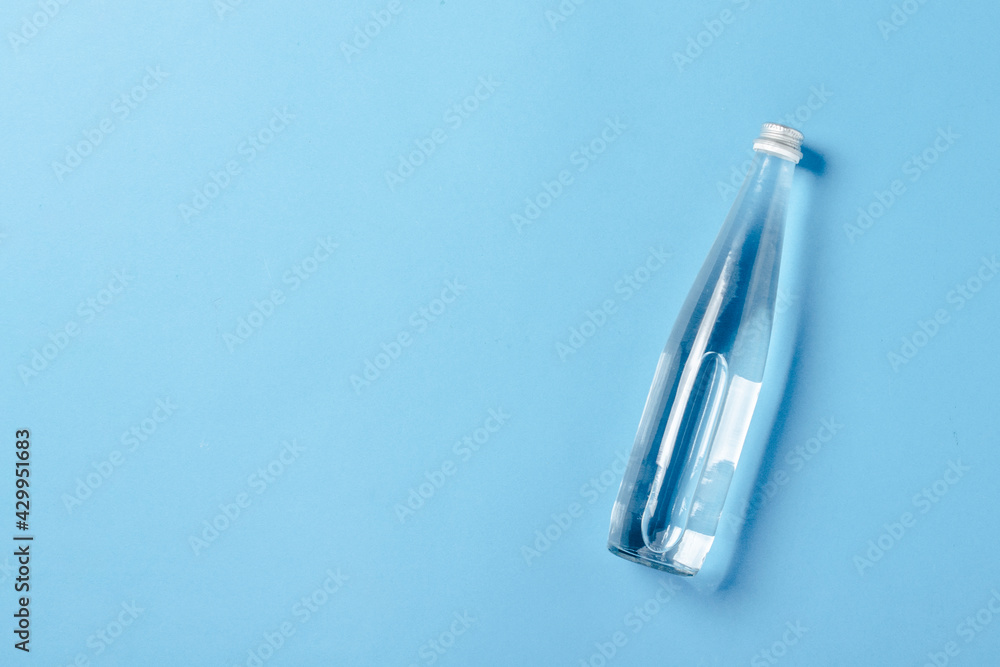 Glass bottle with clear water on a blue background. Concept of health and beauty, water balance, thirst, heat, summer. Flat lay, top view Glass bottle with clear water on a blue background. Concept of health and beauty, water balance, thirst, heat, summer. Flat lay, top view