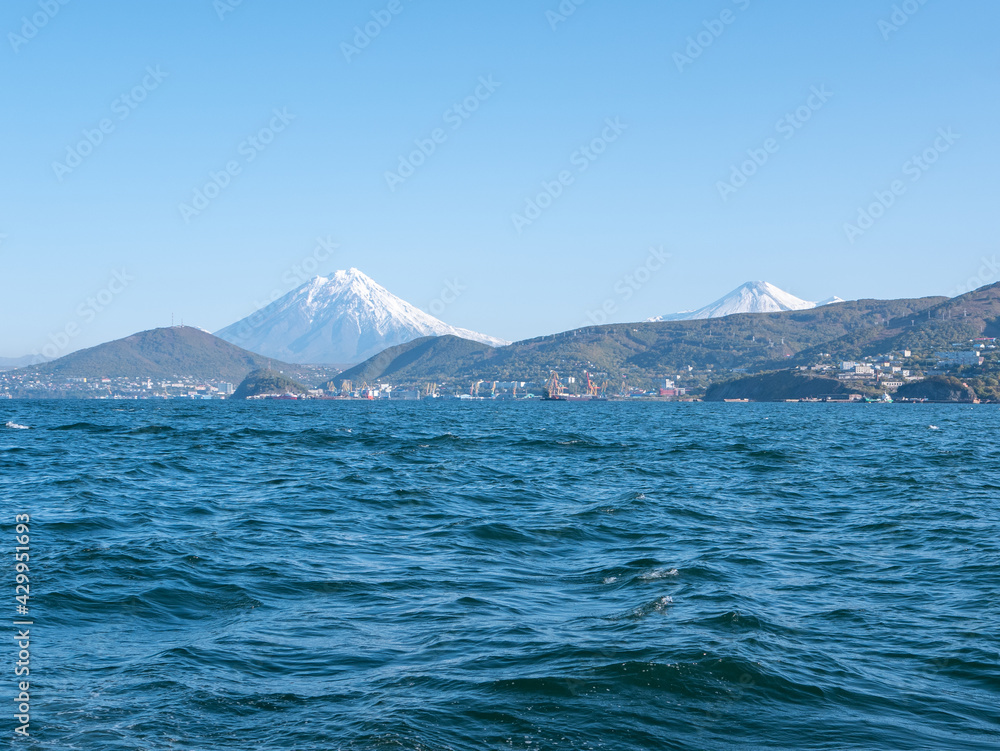 The seaport in the Avacha Bay of Petropavlovsk-Kamchatsky. View from the sailing yacht to the seaport, volcanoes, autumn hills against the blue sky. Kamchatka Peninsula, Russia.