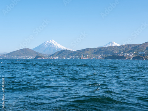 The seaport in the Avacha Bay of Petropavlovsk-Kamchatsky. View from the sailing yacht to the seaport, volcanoes, autumn hills against the blue sky. Kamchatka Peninsula, Russia.