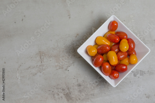 red and yellow small tomatoes in white square bowl. Flatly 