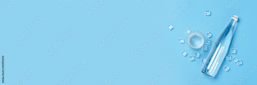 Glass bottle and glass with clear water on a blue background with Ice cubes. Concept of health and beauty, water balance, thirst, heat, summer. Flat lay, top view. Banner Glass bottle and glass with clear water on a blue background with Ice cubes. Concept of health and beauty, water balance, thirst, heat, summer. Flat lay, top view. Banner