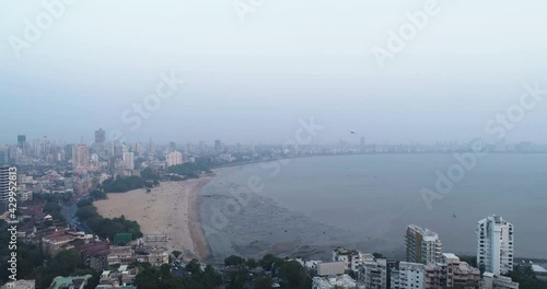 A cinematic drone shot of the famous Marine Drive Chaupati Beach point in South Bombay region of Mumbai City, overlooking the hanging garden hill and forest in a slow smooth motion. photo