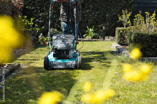 A person with a lawn mower in a garden. Mowing grass in spring and summer. Gardening work.