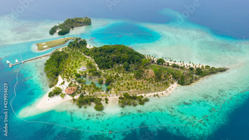 Aerial view of Tropical island with sand beach, palm trees by atoll with coral reef. Malipano island, Philippines, Samal.