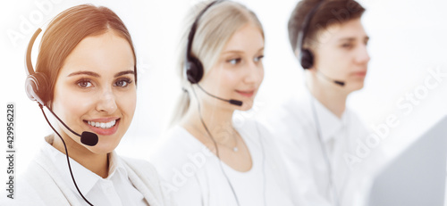 Call center in sunny office. Group of diverse operators at work. Beautiful woman in headset communicating with customers of telemarketing service photo