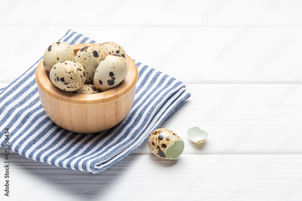 Quail eggs in wooden bowl and napkin on white wooden table. Copy space.