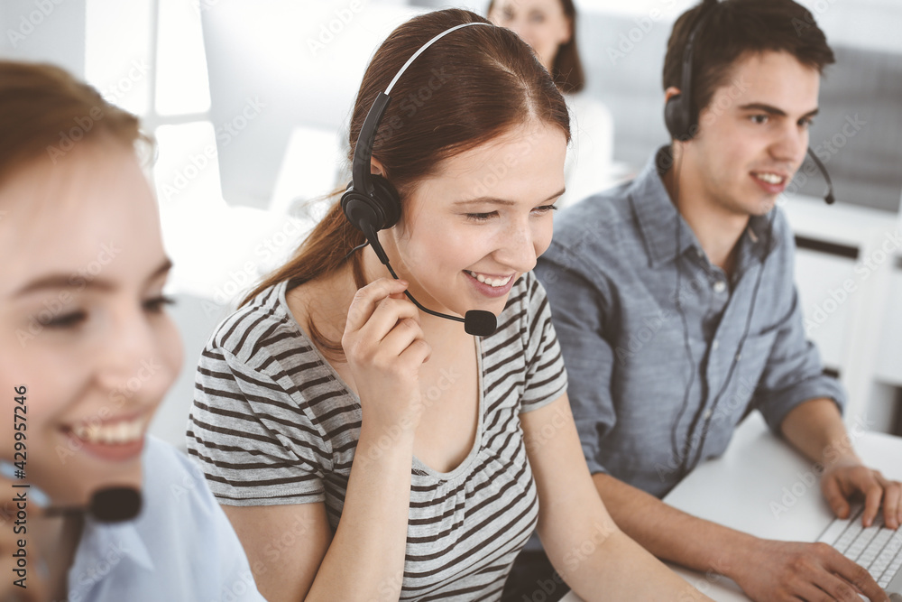 Casual dressed young woman using headset and computer while talking with customers online. Group of operators at work. Call center, business concept Casual dressed young woman using headset and computer while talking with customers online. Group of operators at work. Call center, business concept