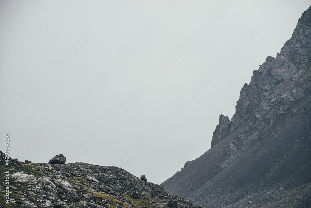 Atmospheric highlands landscape with narrow mountain valley and sharp rocks on steep slope under gray sky. Bleak mountain scenery with pointed rockies on mountainside and glen in overcast weather.