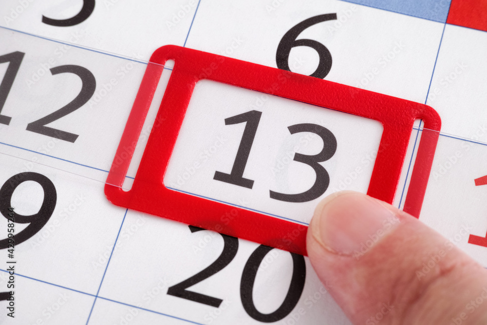 A finger pointing at the 13th day of the month on a calendar A finger pointing at the 13th day of the month on a calendar