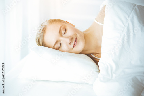 Happy woman sleeping in bedroom comfortably and blissfully. Waking up in sunny morning