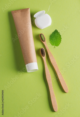 Two bamboo toothbrushes, toothpaste, dental floss and a leaf on green