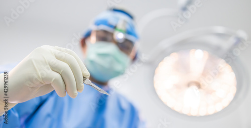 Obraz na plátne Close up of surgeon's hand holding a scalpel and blurred male doctor's face on background with copy space