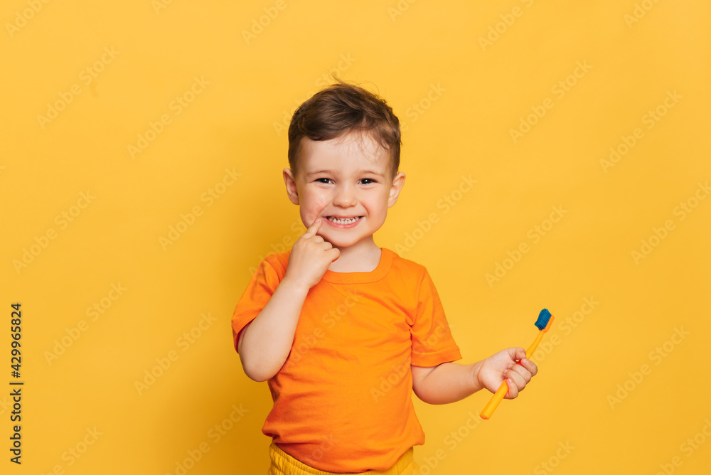 Happy baby toddler boy brushing his teeth with a toothbrush on a yellow background. Health care, oral hygiene. Happy baby toddler boy brushing his teeth with a toothbrush on a yellow background. Health care, oral hygiene.